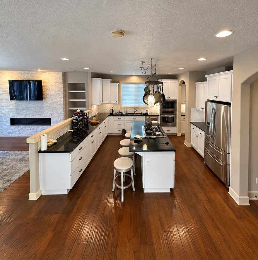 After cabinet painting: white kitchen cabinets and island with dark countertops and black handles.