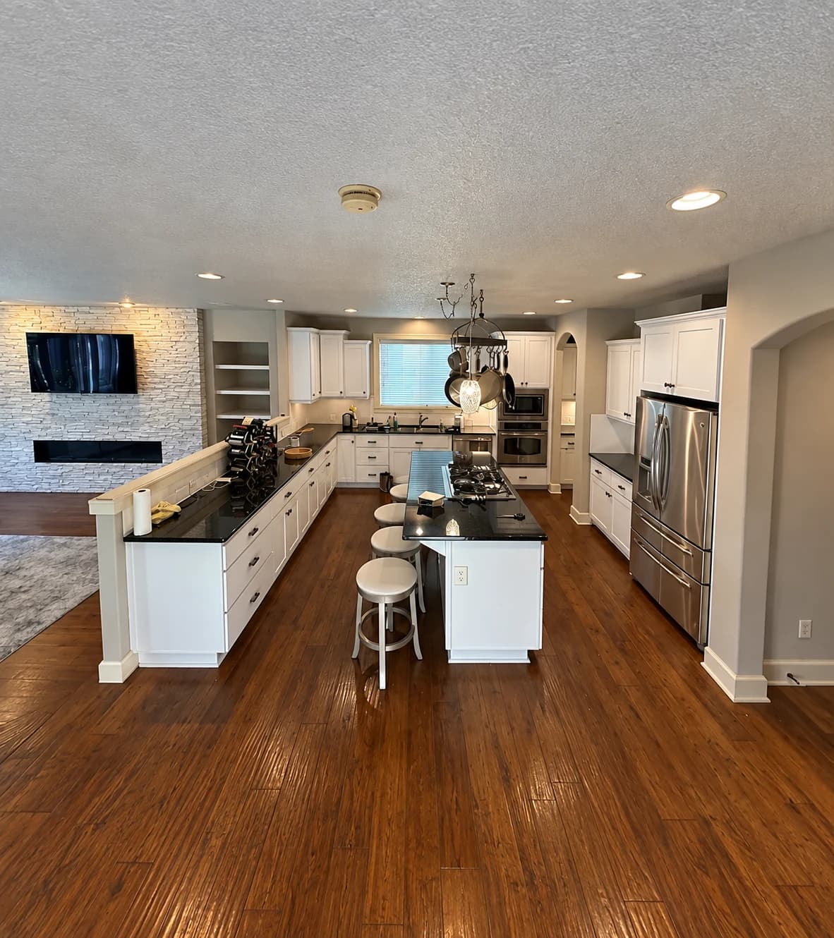 After cabinet painting: white kitchen cabinets and island with dark countertops and black handles.