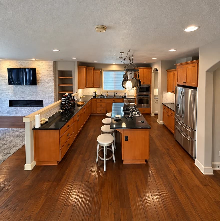 Before cabinet painting: wood-finish kitchen cabinets and island with dark countertops and black handles.